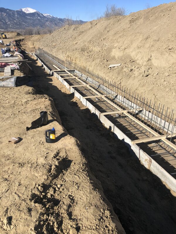 Concrete footing formwork and rebar cage in an excavated trench with Pikes Peak in the distance